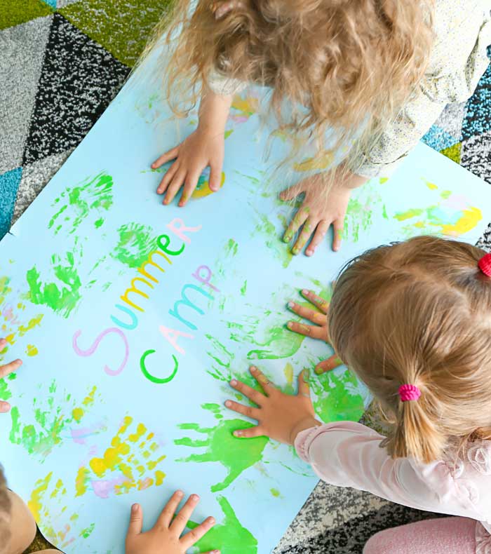 Dos niñas dejando pintando con las huellas con sus manos en un cartel de summer camp